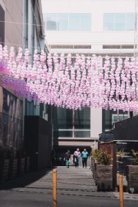 Colorful alley in Melbourne with pink decorations and people walking under a sunny sky.