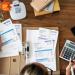 Personne examinant des documents financiers et gérant des factures impayées avec une calculatrice.