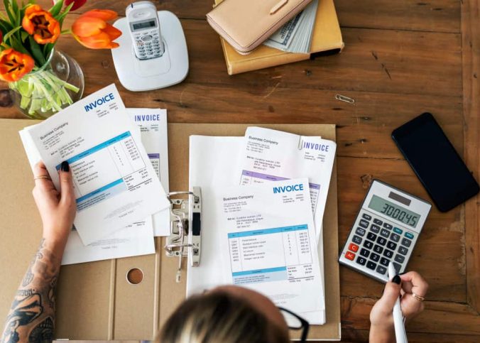 Personne examinant des documents financiers et gérant des factures impayées avec une calculatrice.