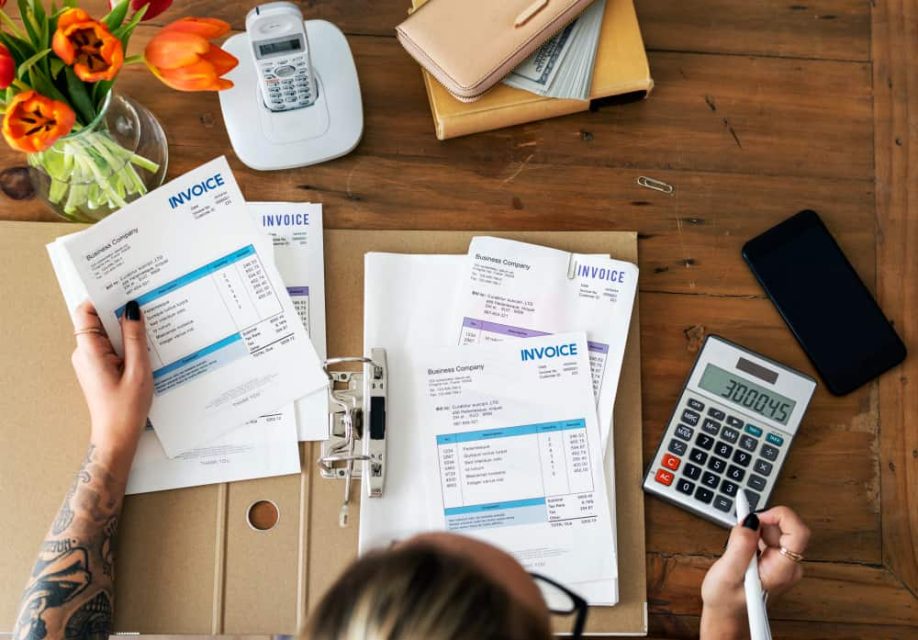 Personne examinant des documents financiers et gérant des factures impayées avec une calculatrice.