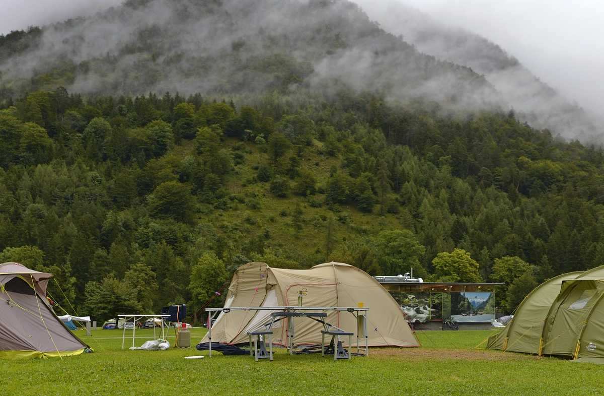 Plusieurs tentes beige et verte dressées dans prairie avec montagnes boisées brumeux à l'arrière-plan Plusieurs tentes beige et verte dressées dans prairie avec montagnes boisées brumeux à l'arrière-plan