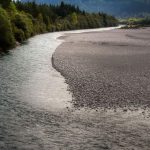 Rivière sinueuse bordée de forêt et de plage, montagnes en arrière-plan