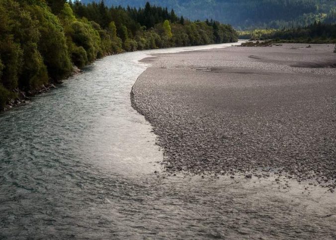 Rivière sinueuse bordée de forêt et de plage, montagnes en arrière-plan