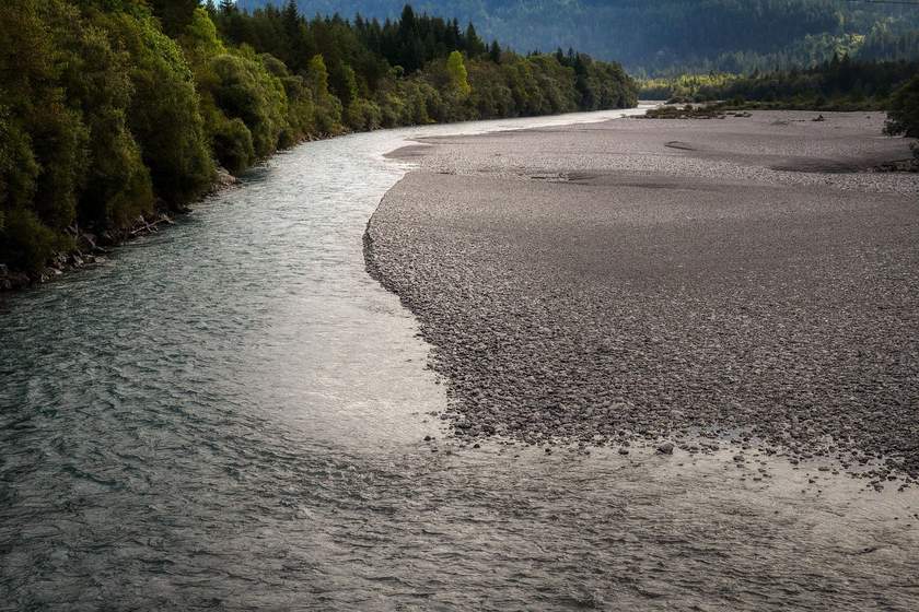 Rivière sinueuse bordée de forêt et de plage, montagnes en arrière-plan