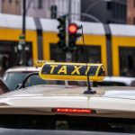 Taxi blanc stationné dans une rue urbaine avec feu rouge et tramway jaune derrière