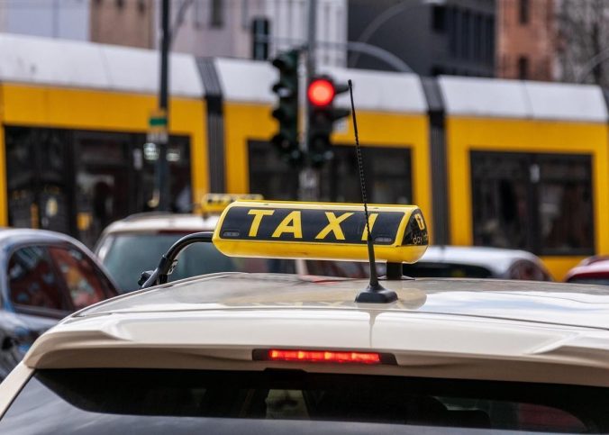 Taxi blanc stationné dans une rue urbaine avec feu rouge et tramway jaune derrière