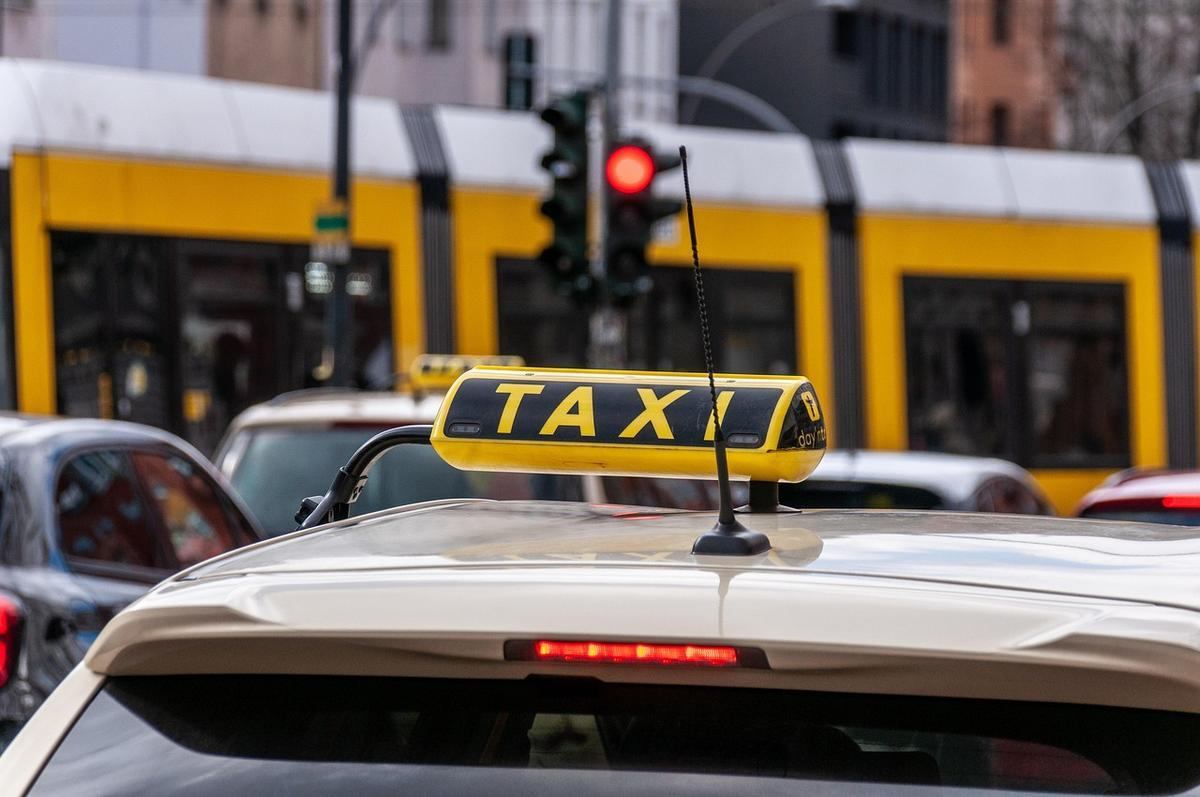 Taxi blanc stationné dans une rue urbaine avec feu rouge et tramway jaune derrière