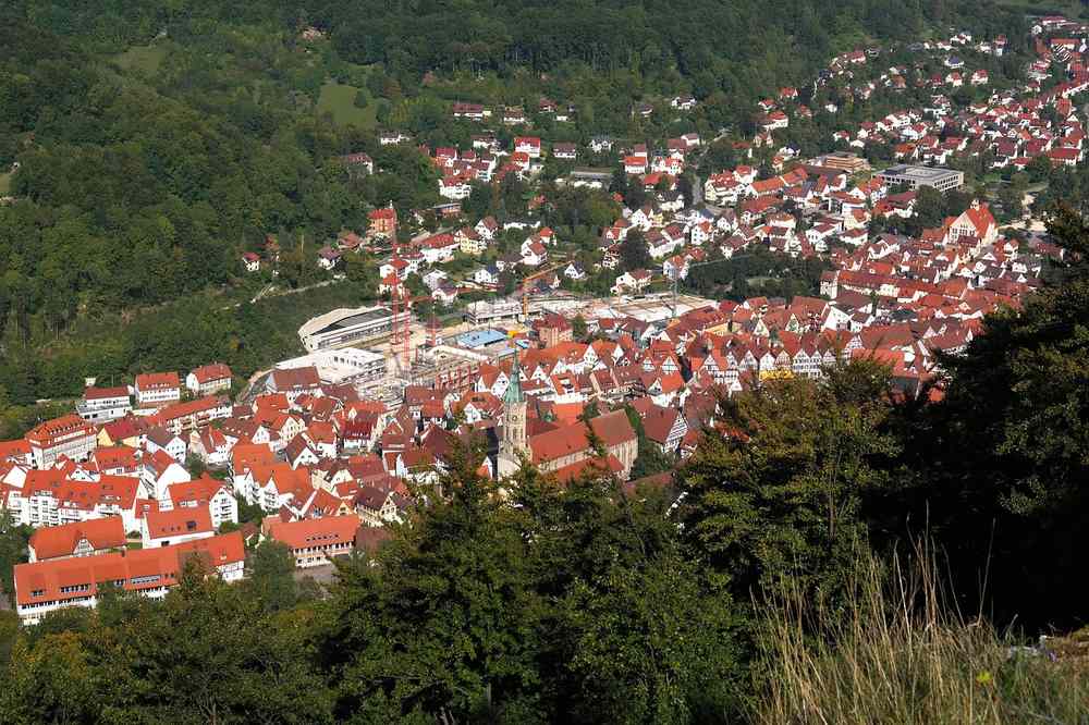 Une ville aux toits rouges s'étale au creux d'une vallée boisée Une ville aux toits rouges s'étale au creux d'une vallée boisée