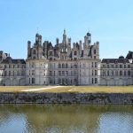 Un château Renaissance se reflète dans l'eau sous un ciel clair