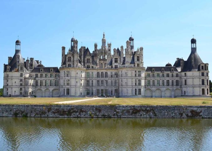 Un château Renaissance se reflète dans l'eau sous un ciel clair