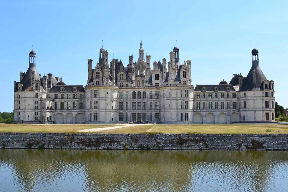 Un château Renaissance se reflète dans l'eau sous un ciel clair