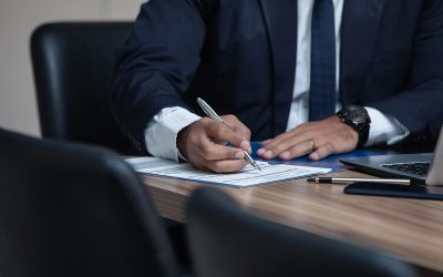 Homme en costume noir écrivant sur une feuille à une table en bois