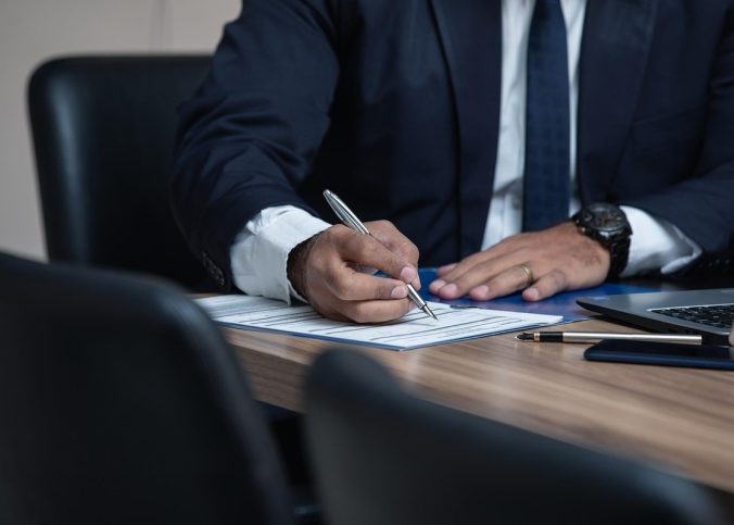 Homme en costume noir écrivant sur une feuille à une table en bois