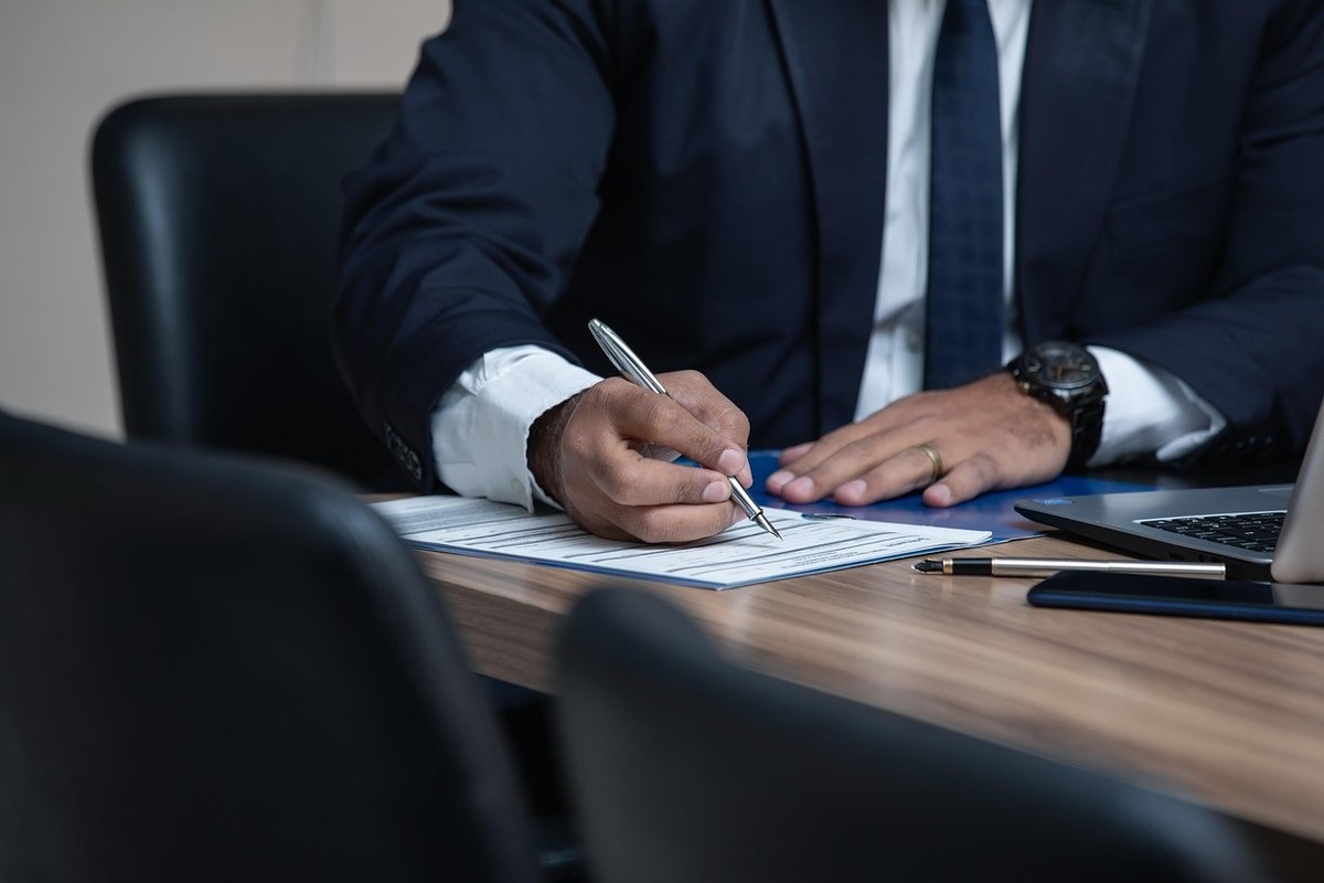Homme en costume noir écrivant sur une feuille à une table en bois