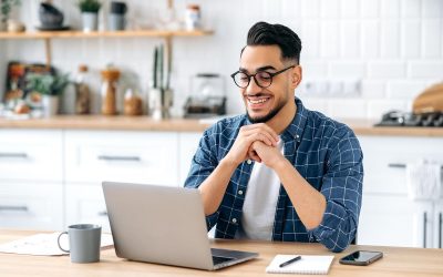 Un jeune homme souriant, lunettes, chemise à carreaux, devant son ordinateur