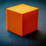 Un cube orange cubeux posé sur un fond bleu sombre