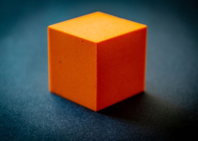 Un cube orange cubeux posé sur un fond bleu sombre