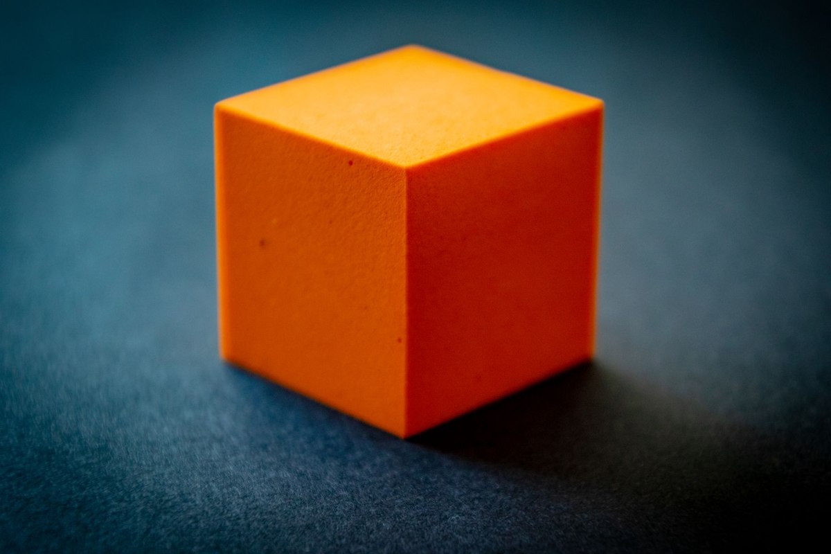 Un cube orange cubeux posé sur un fond bleu sombre